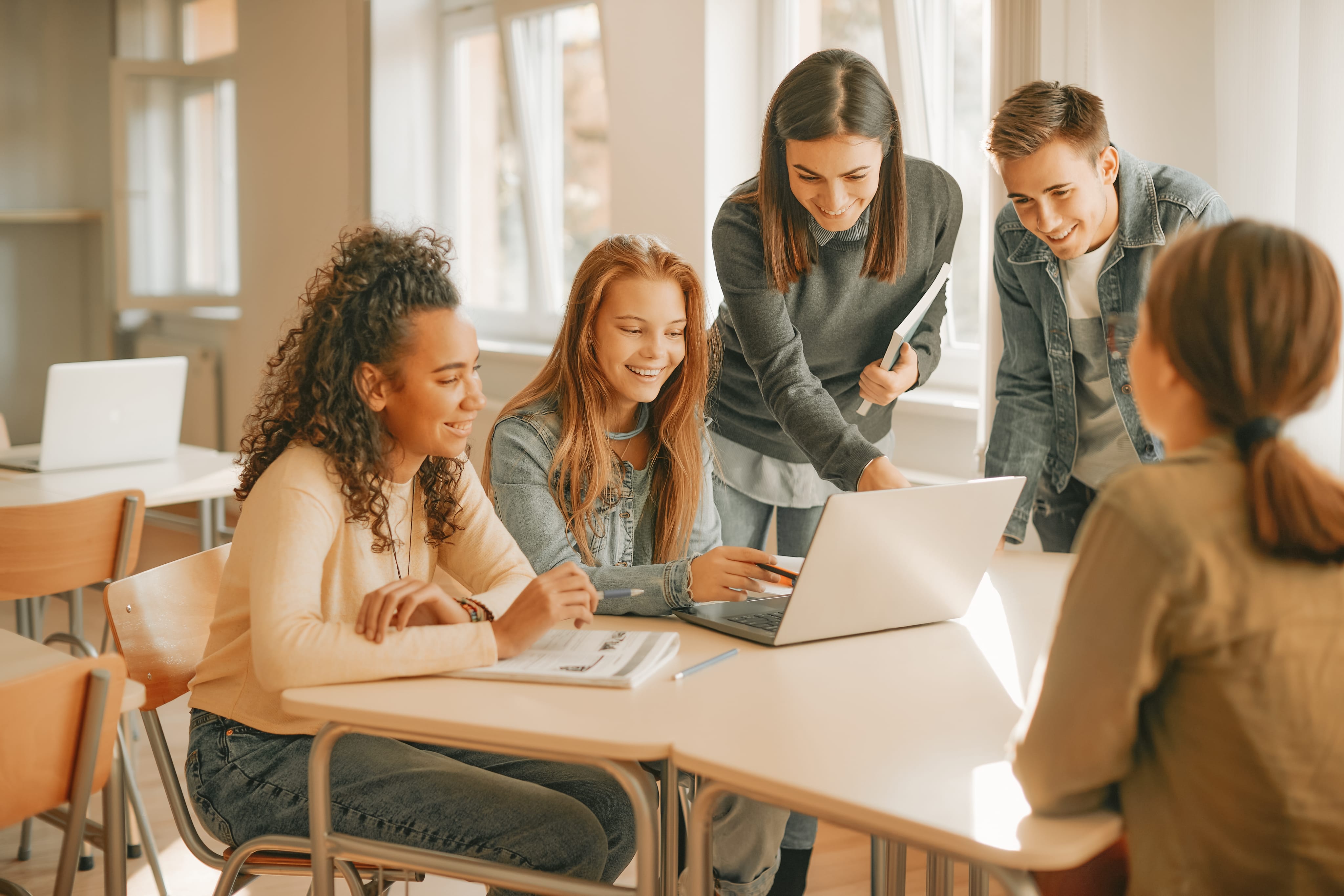 group of students reviewing information on laptop at a table with their teacher