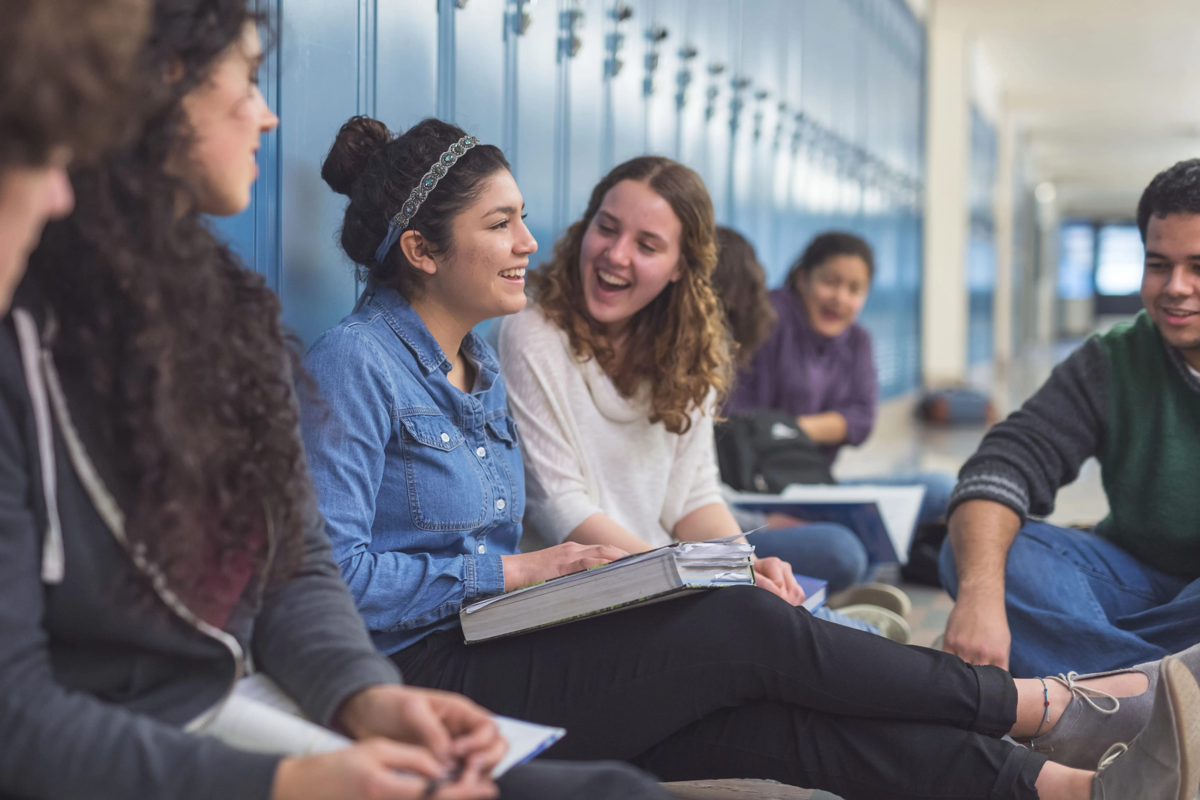 group of students sitting in a hallway against lockers